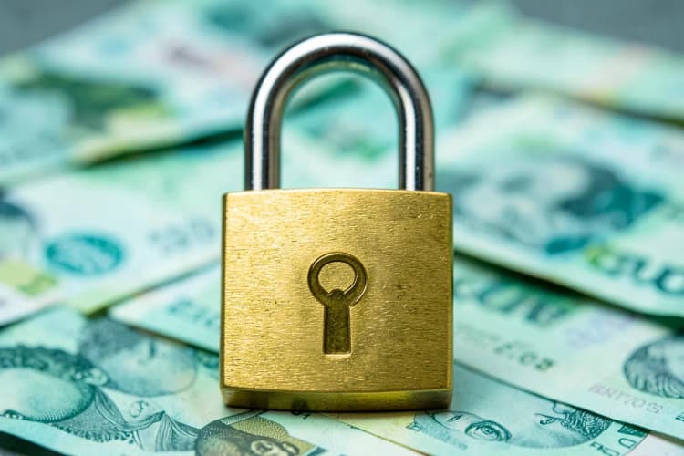 Um close-up de um cadeado dourado com o símbolo da Shopee em relevo, sobre um fundo desfocado de notas de dinheiro.