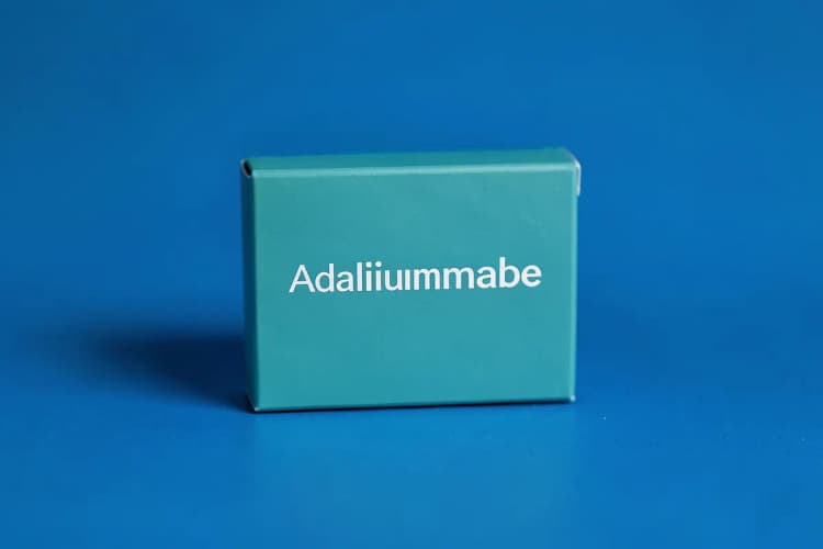 Uma caixa de medicamento com o nome "Adalimumabe" em destaque sobre um fundo azul.