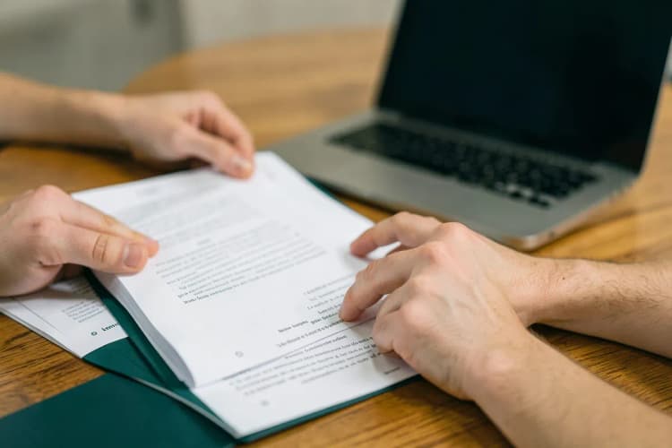 Advogado analisando documentos em uma mesa com um laptop aberto, plano detalhe nas mãos e papéis.