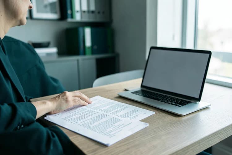 Advogado revisando papéis em uma mesa com um laptop, plano médio mostrando a interação com os documentos.