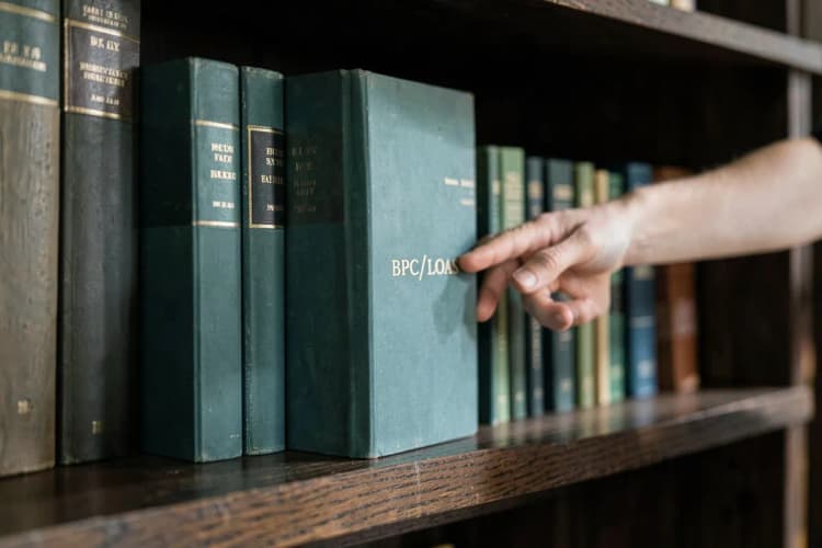 Uma pessoa escolhendo entre várias opções de livros de direito em uma estante, com foco em um livro com a sigla BPC/LOAS.