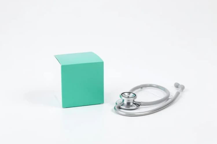 Uma caixa de medicamento genérico ao lado de um estetoscópio sobre uma superfície branca.