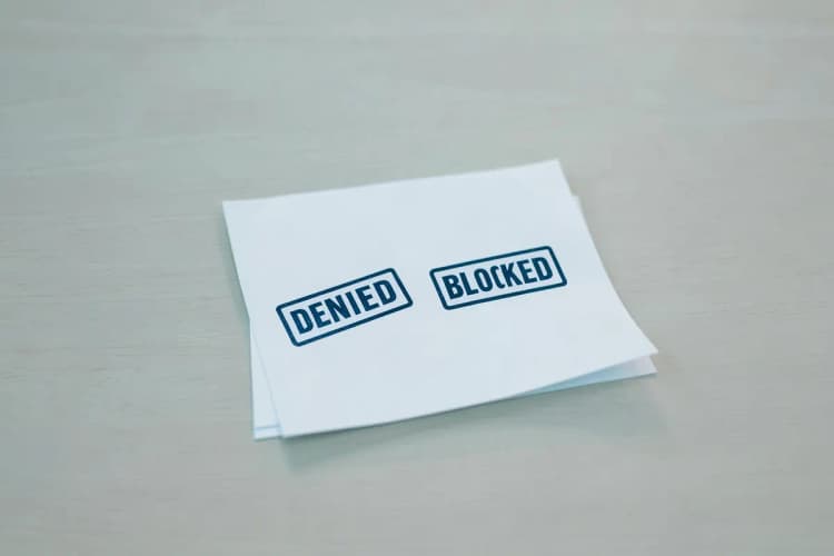 Um documento com carimbos de "negado" e "bloqueado" sobre uma mesa.