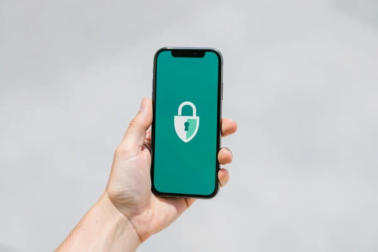 Uma mão segurando um celular com a tela mostrando um ícone de cadeado e um escudo.