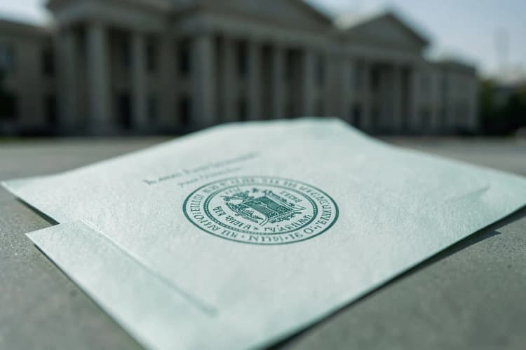 Uma mão segurando um documento com um selo oficial, com um fundo desfocado de um prédio governamental.