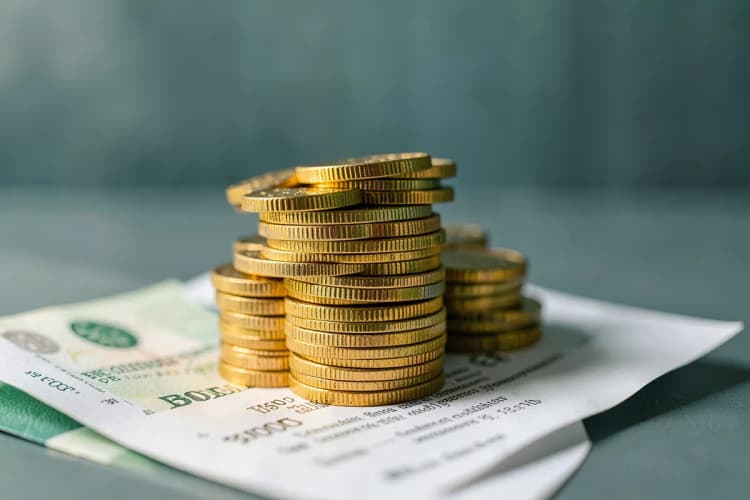 Uma pilha de moedas de ouro e notas de dinheiro empilhadas em cima de um contrato imobiliário.