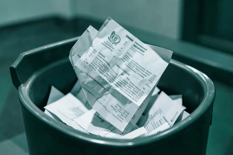 Uma mão jogando um contrato de time-share amassado em uma lixeira cheia de papéis.