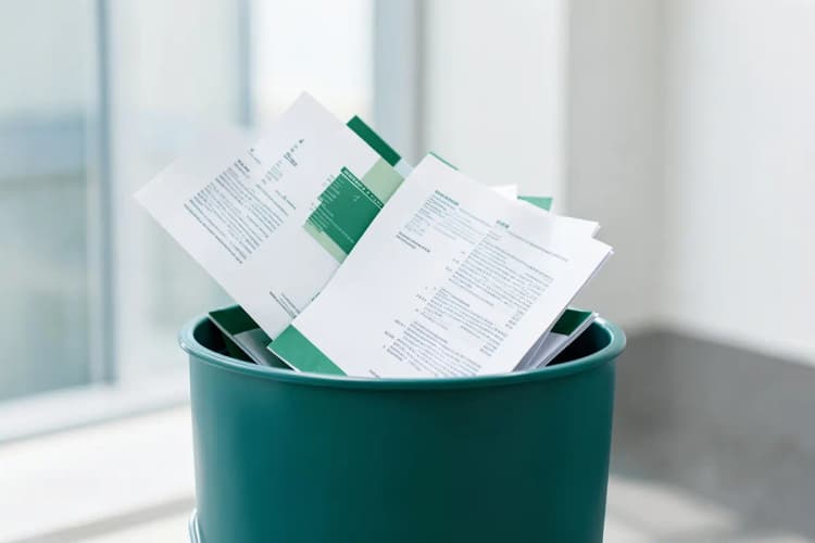 Uma pessoa jogando papéis e documentos em uma lixeira, simbolizando o cancelamento.