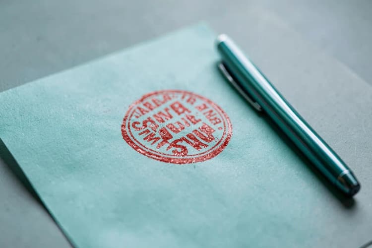 Um documento com um carimbo vermelho e uma caneta ao lado, em plano detalhe.