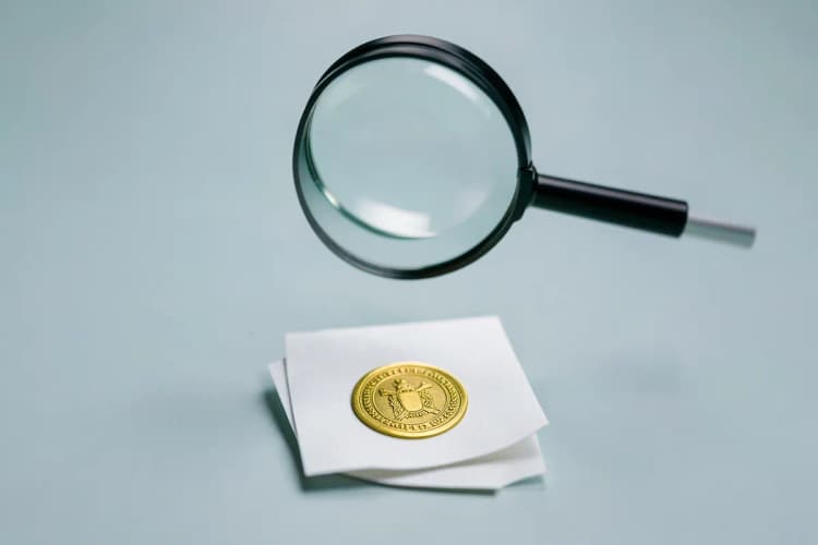 Uma lupa examinando um pequeno pedaço de papel com um selo dourado.